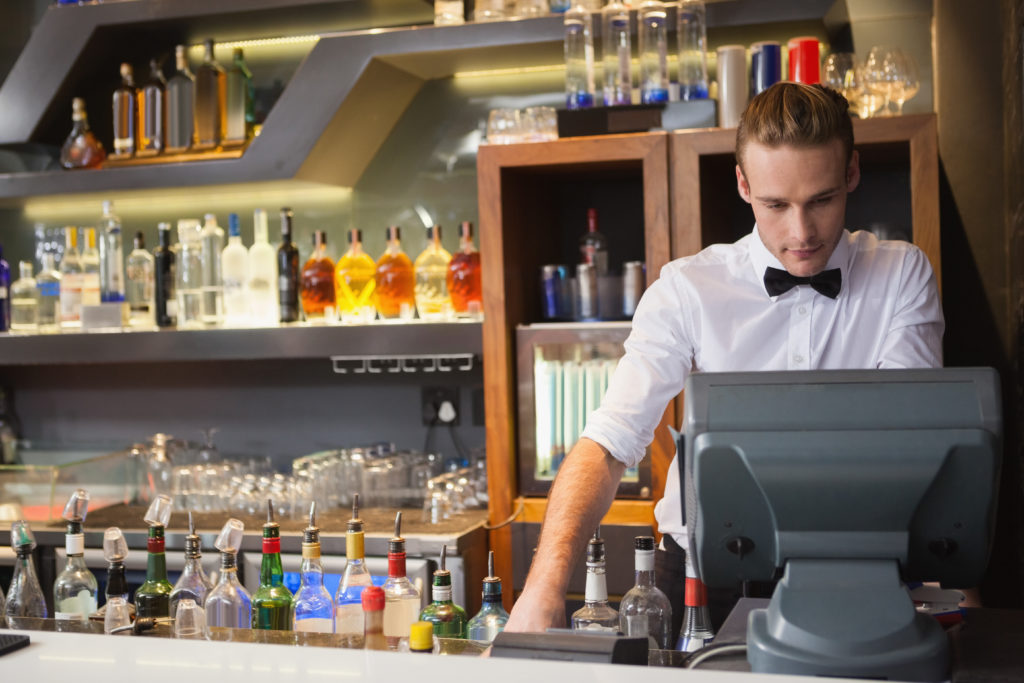 Jeune barman derrière une caisse enregistreuse dans un bar